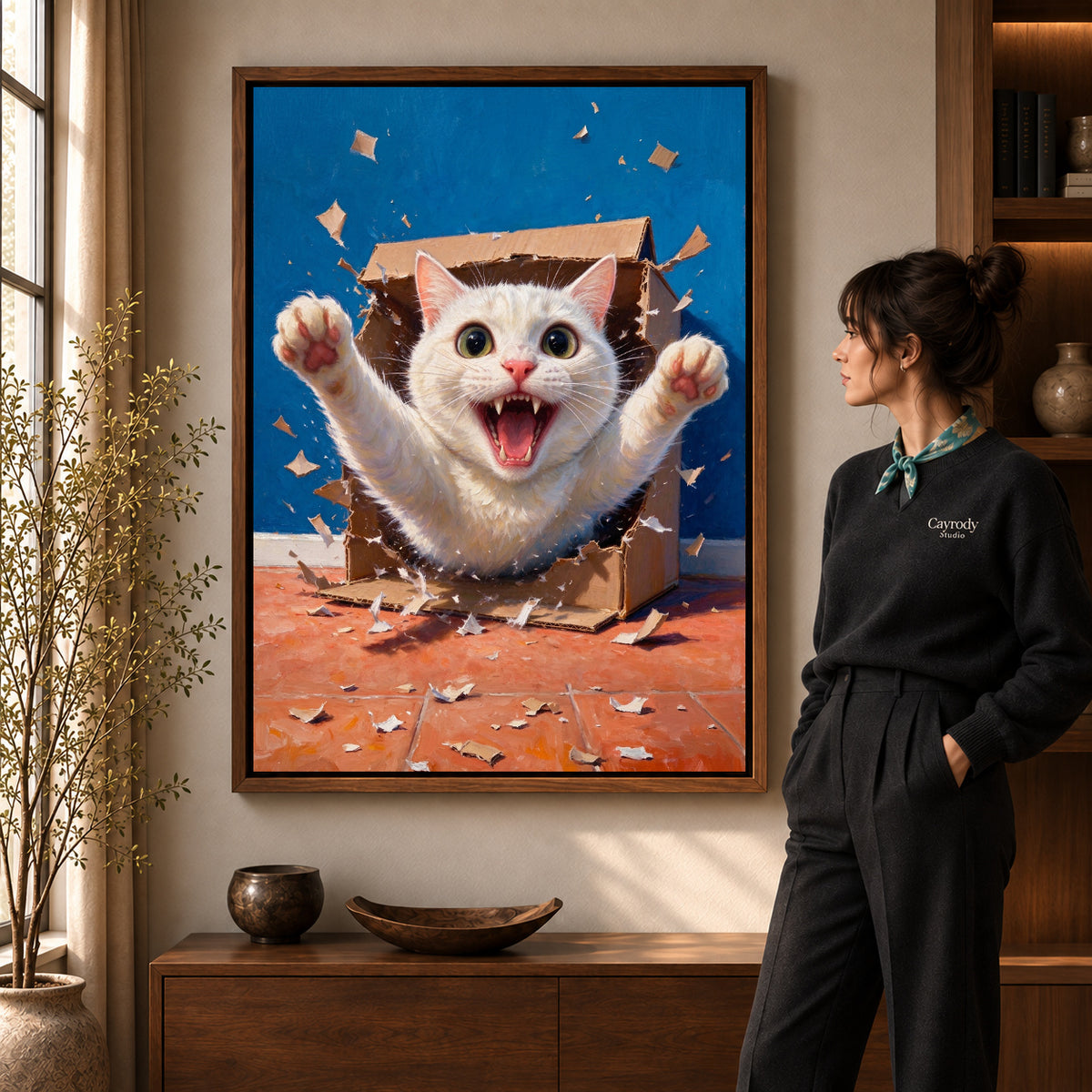 Surprise Box Kitten artwork in a walnut frame beside a standing woman in a warm room.