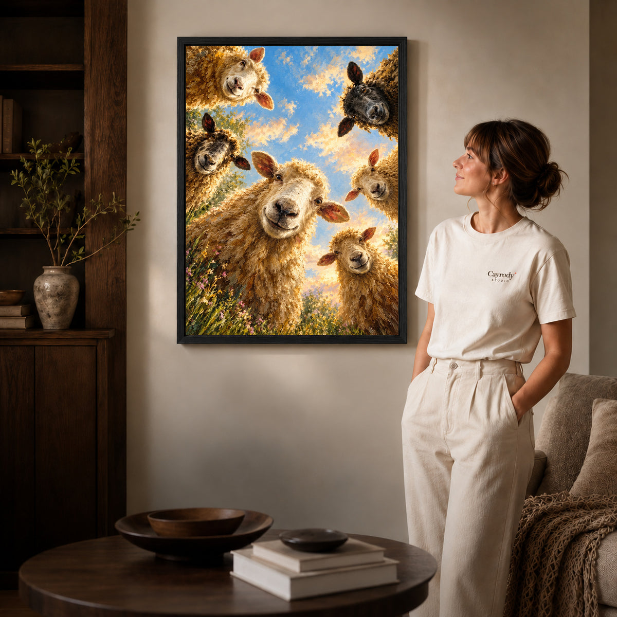 Black framed sheep selfie friends artwork beside a woman in a warm neutral living room.