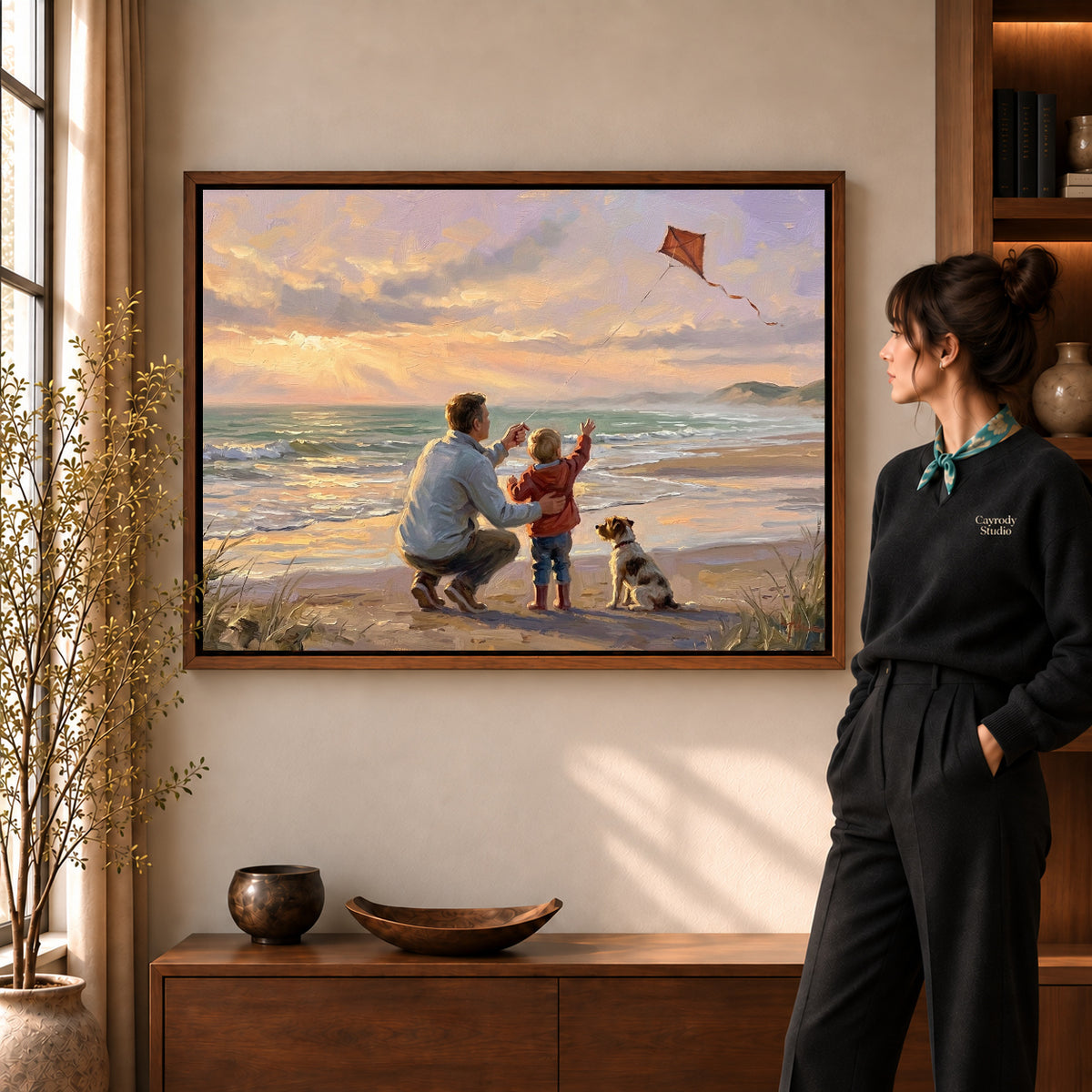 Family Beach Kite artwork in a walnut frame beside a standing woman in a warm room.