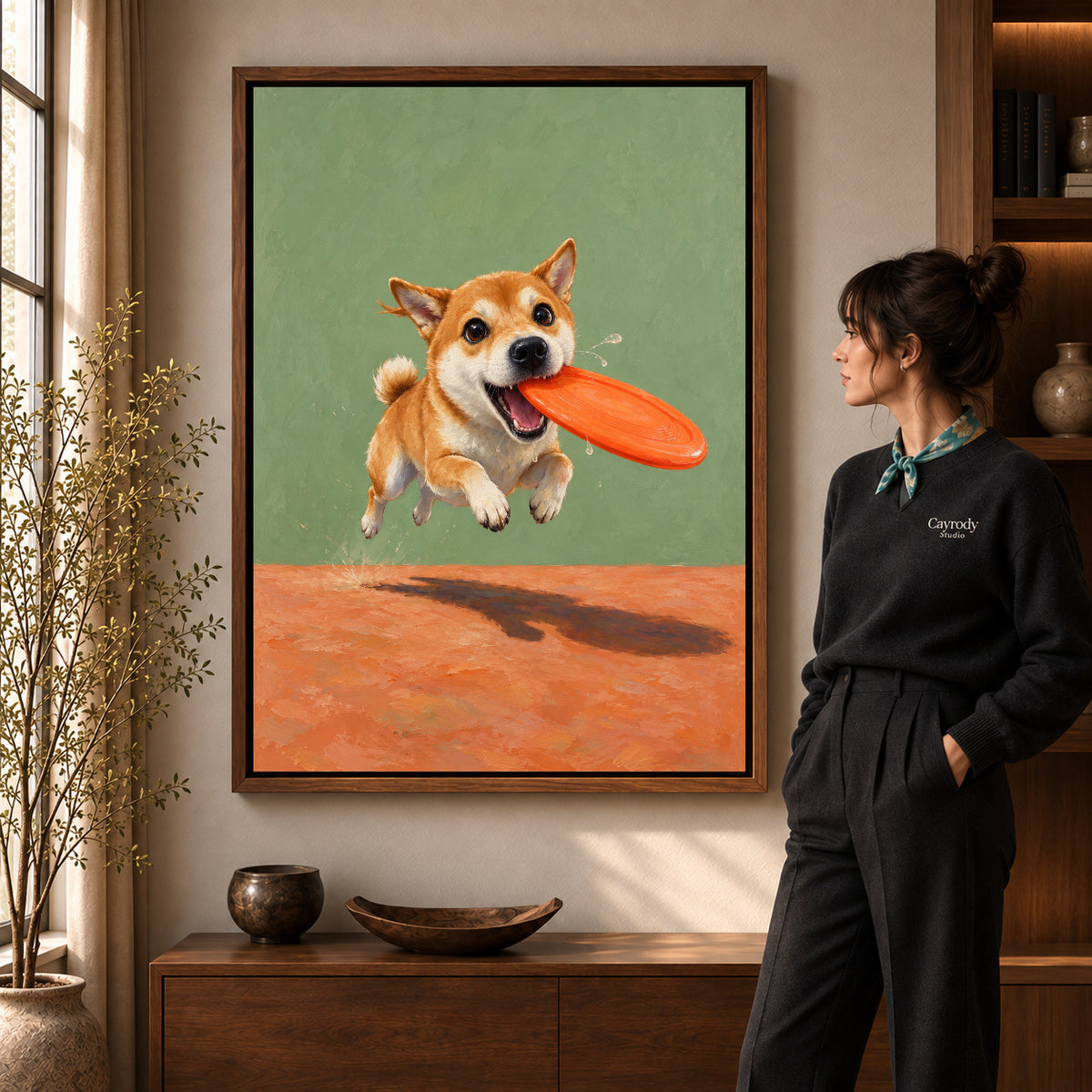 Flying Disc Puppy artwork in a walnut frame beside a standing woman in a warm room.
