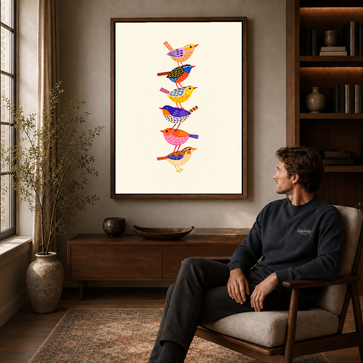 Walnut framed stacked folk birds artwork above a seated man in a wood furnished living room.