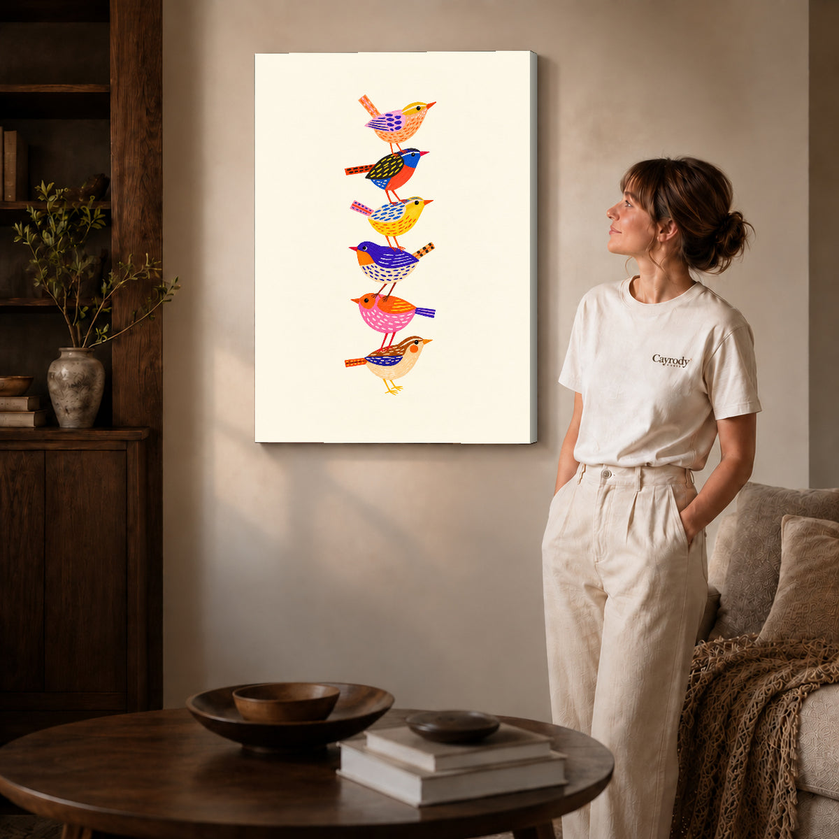 Gallery wrapped stacked folk birds artwork with shaded canvas edges beside a woman wearing cream clothing.