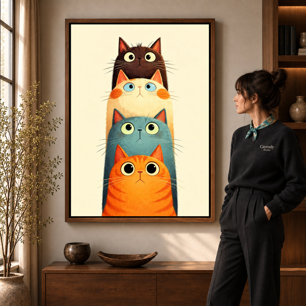 Stacked Curious Cats artwork in a walnut frame beside a standing woman in a warm room.