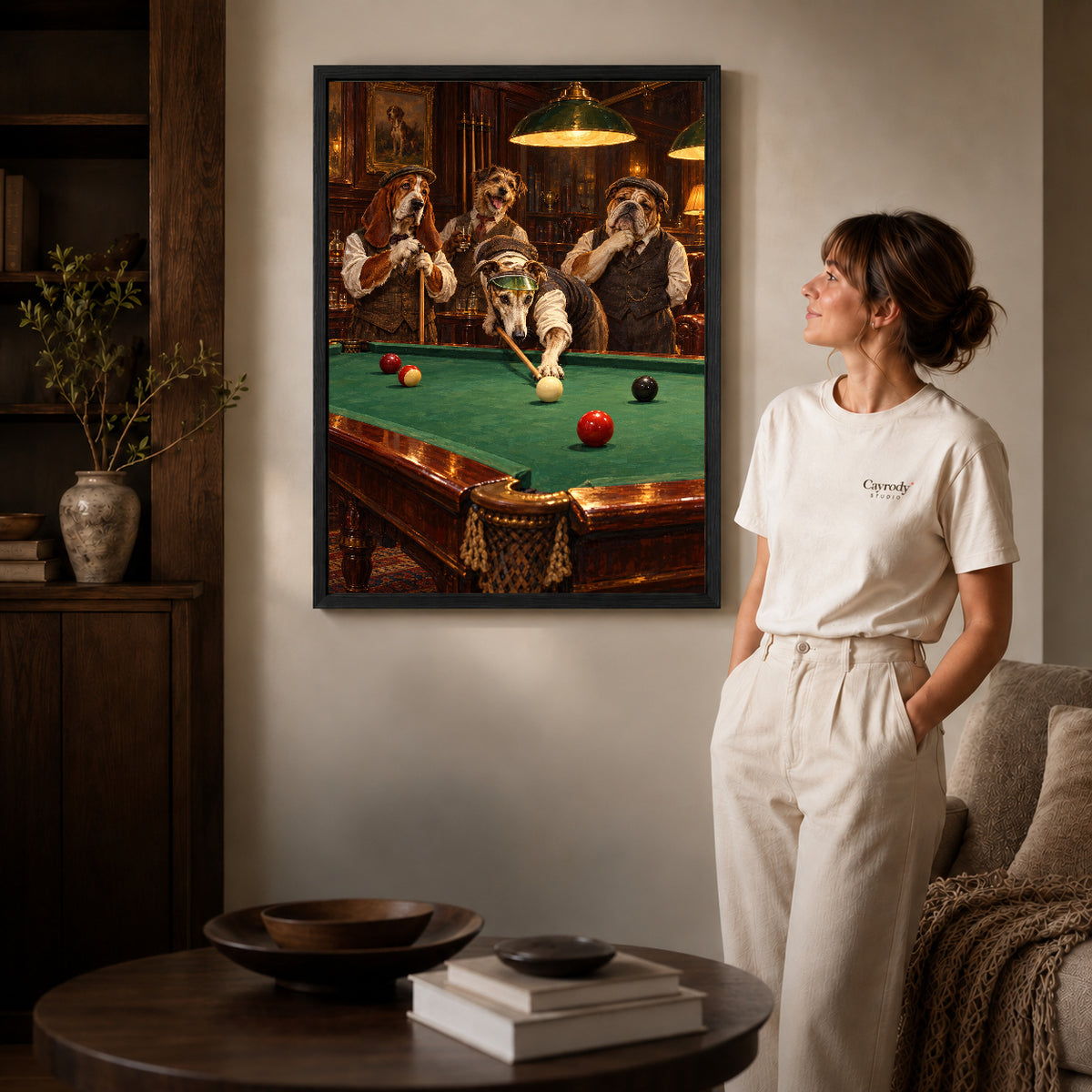 Black framed billiard dog friends artwork beside a woman in a warm neutral living room.