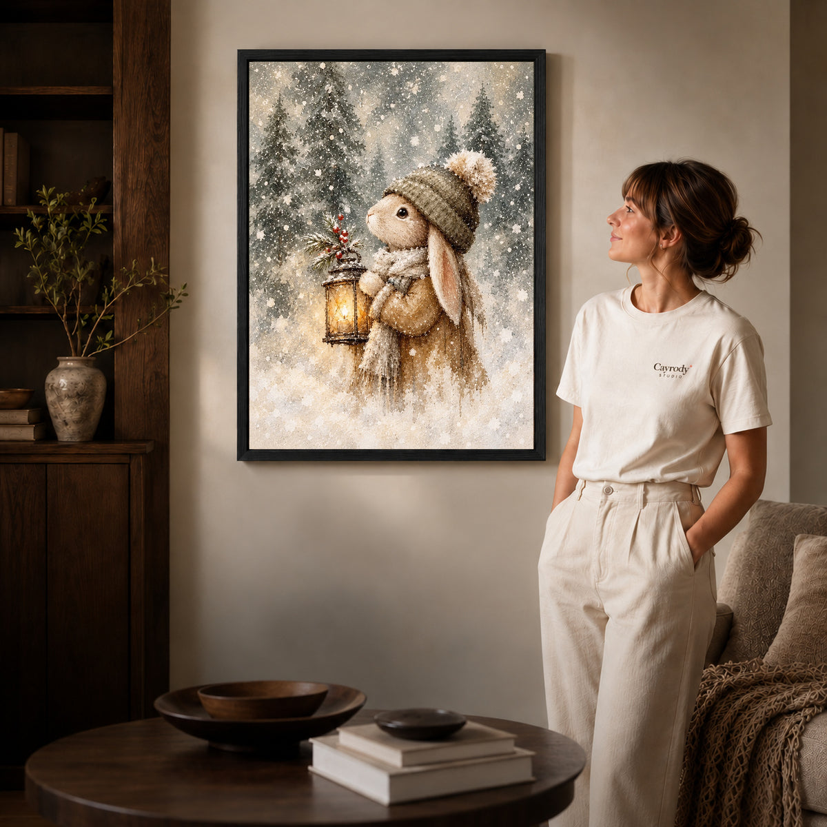 Black framed winter lantern rabbit artwork beside a woman in a warm neutral living room.
