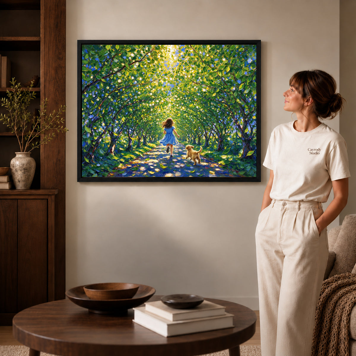 Black framed sunlit woodland run artwork beside a woman in a warm neutral living room.