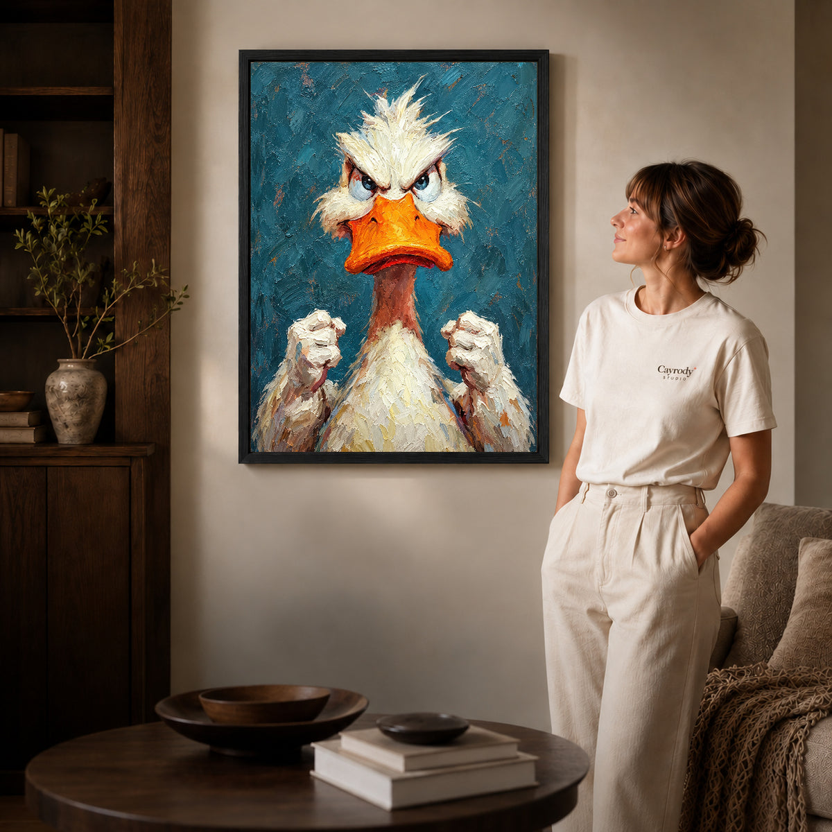 Black framed feisty duck portrait artwork beside a woman in a warm neutral living room.