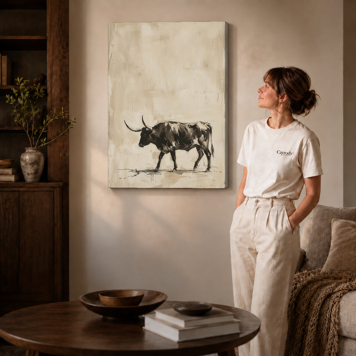 Gallery wrapped neutral longhorn bull artwork with shaded canvas edges beside a woman wearing cream clothing.
