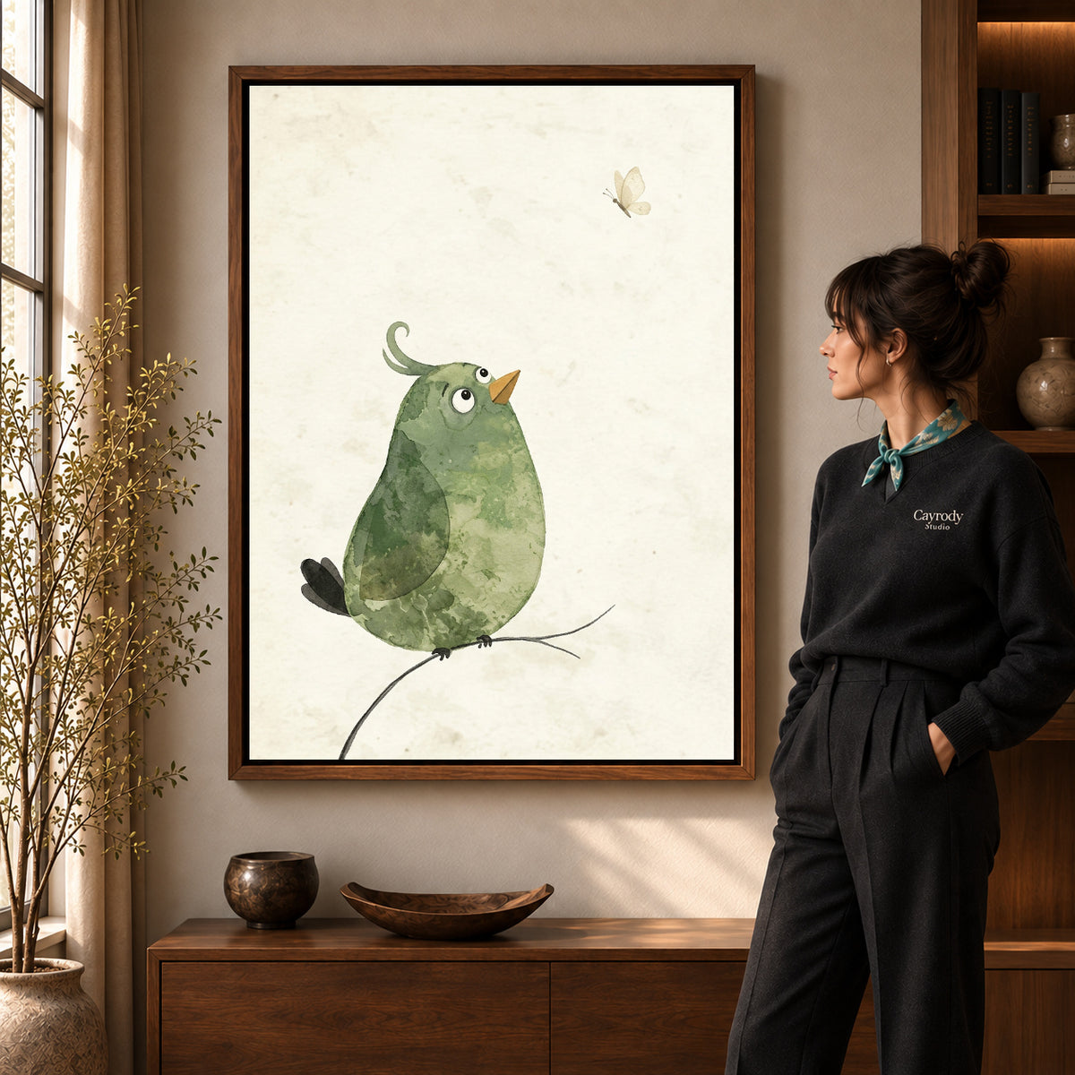Butterfly Watching Bird artwork in a walnut frame beside a standing woman in a warm room.