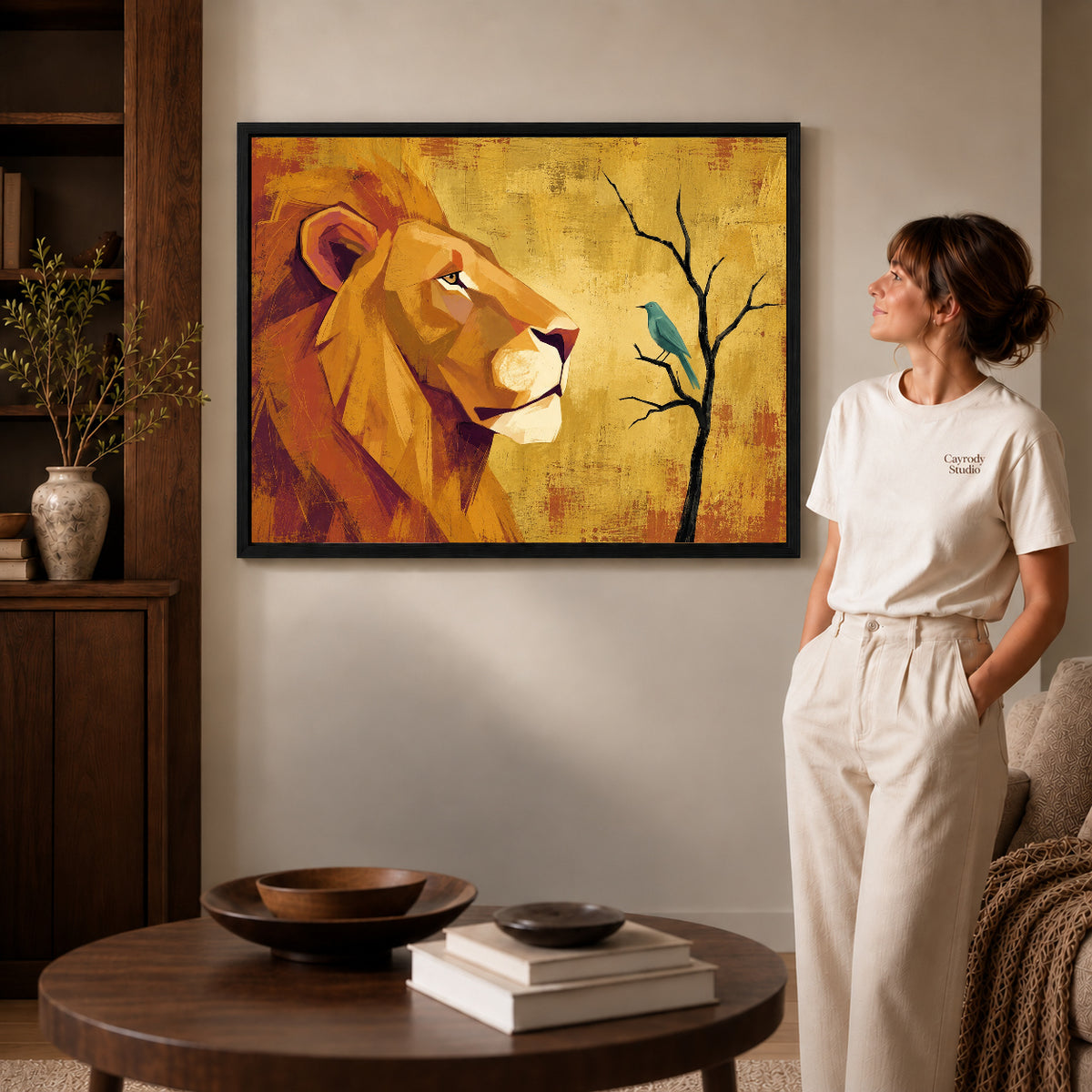 Black framed lion bird encounter artwork beside a woman in a warm neutral living room.