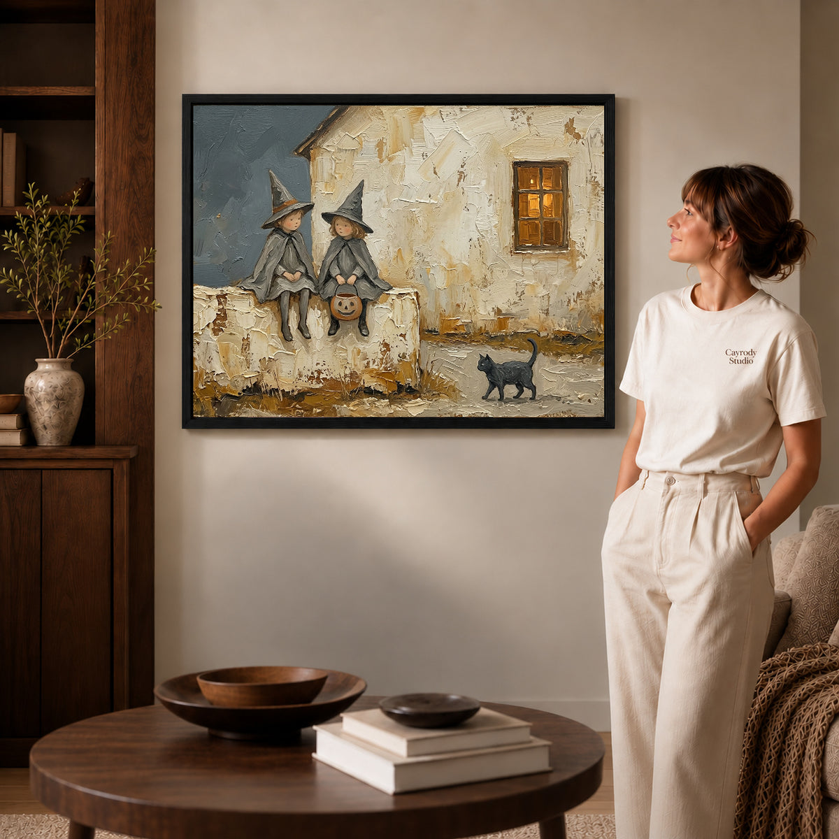 Black framed cottage witch friends artwork beside a woman in a warm neutral living room.