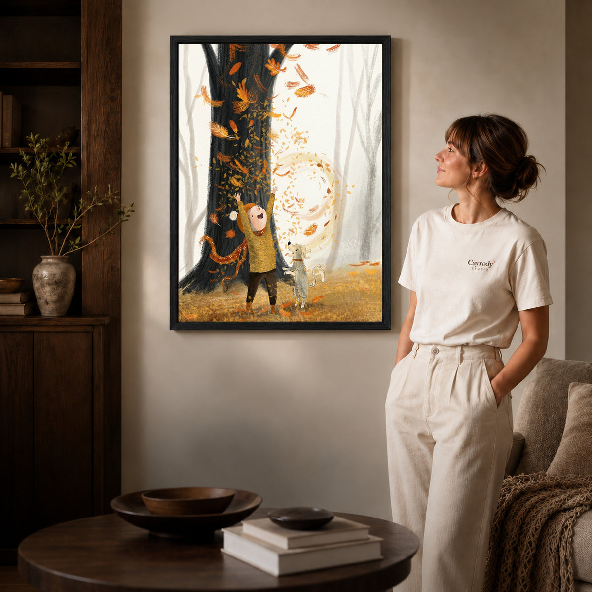 Black framed autumn leaf wonder artwork beside a woman in a warm neutral living room.