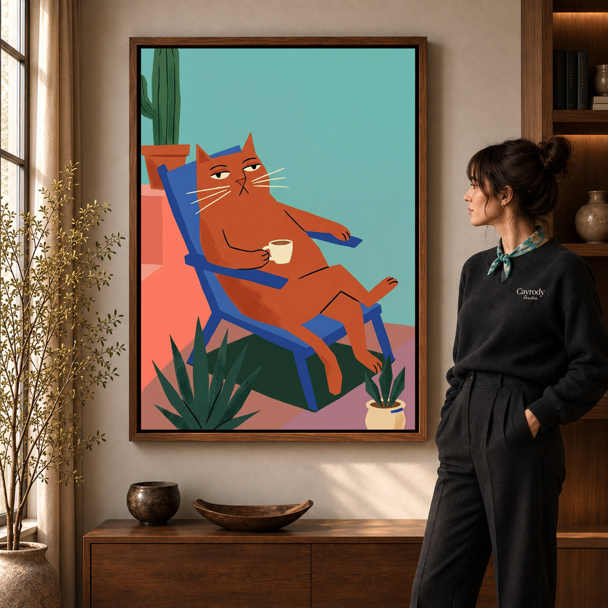 Coffee Break Cat artwork in a walnut frame beside a standing woman in a warm room.