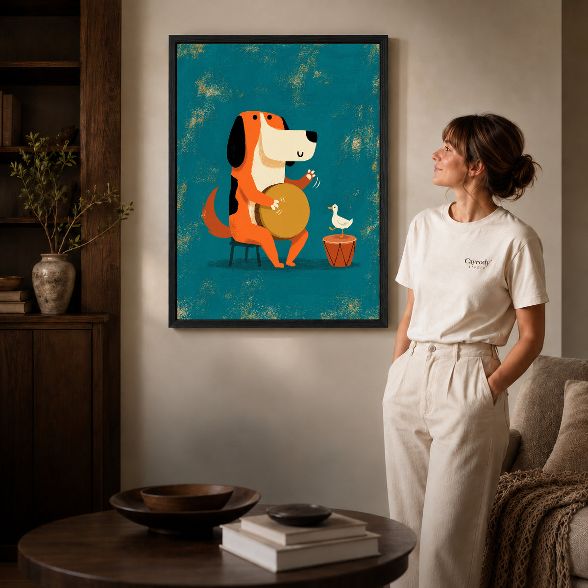 Black framed drumming dog duo artwork beside a woman in a warm neutral living room.