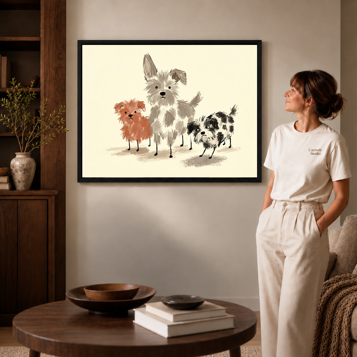 Black framed scruffy dog trio artwork beside a woman in a warm neutral living room.