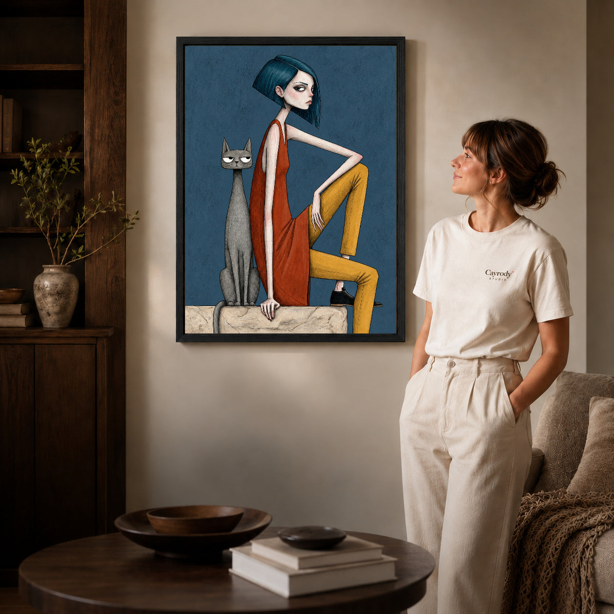 Black framed angular woman cat artwork beside a woman in a warm neutral living room.