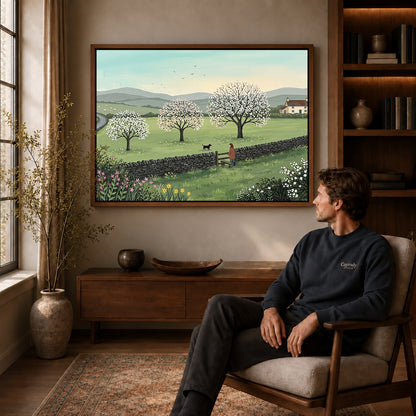 Walnut framed spring meadow walk artwork above a seated man in a wood furnished living room.