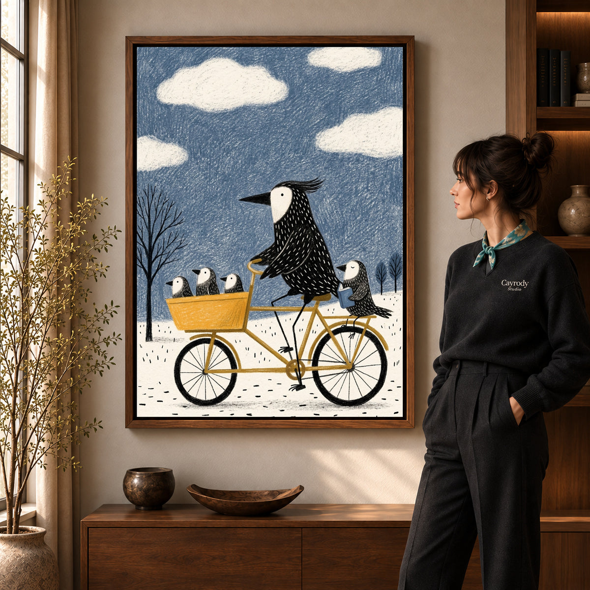 Bicycle Bird Family artwork in a walnut frame beside a standing woman in a warm room.