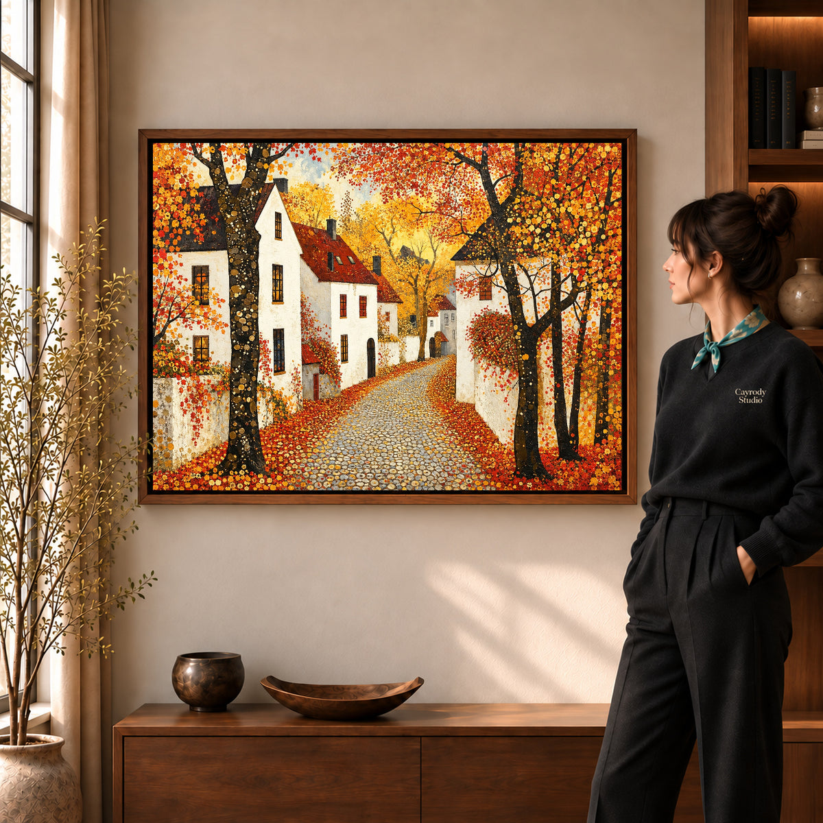 Golden Village Lane artwork in a walnut frame beside a standing woman in a warm room.