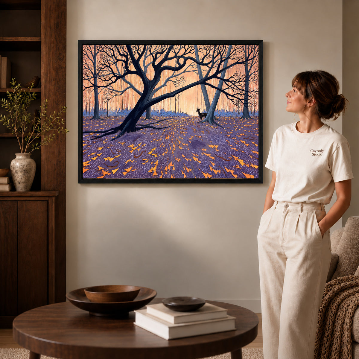 Black framed twilight forest deer artwork beside a woman in a warm neutral living room.