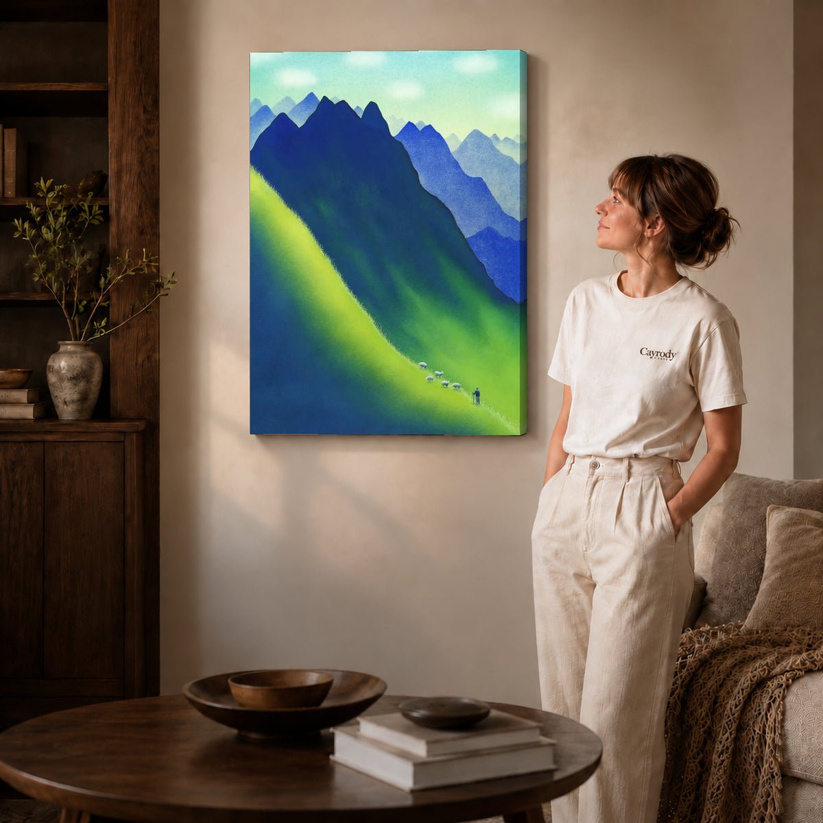 Gallery wrapped blue mountain canvas art with naturally shaded canvas edges beside a woman wearing cream clothing.