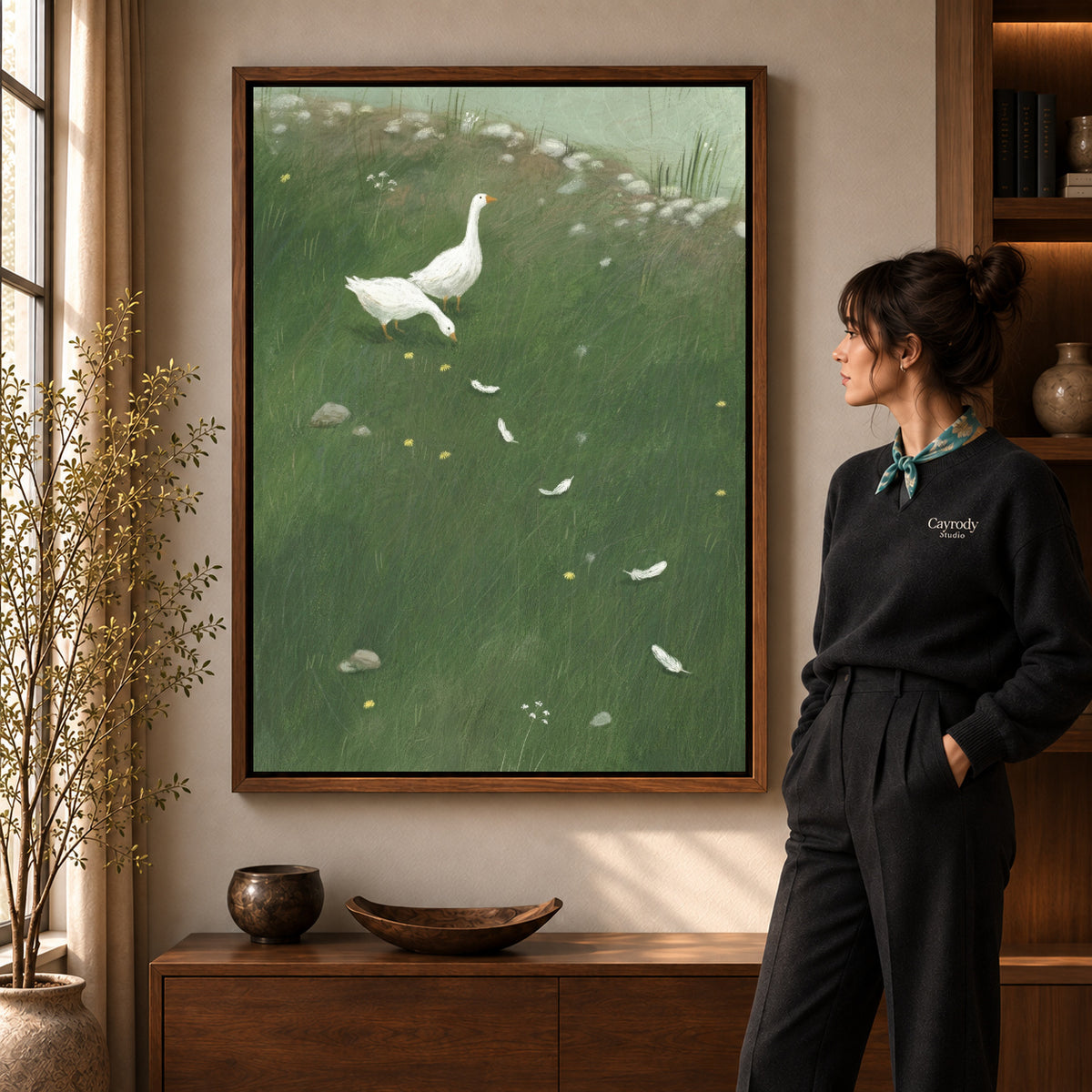White goose meadow canvas art in a walnut frame beside a standing woman in a warm living room.