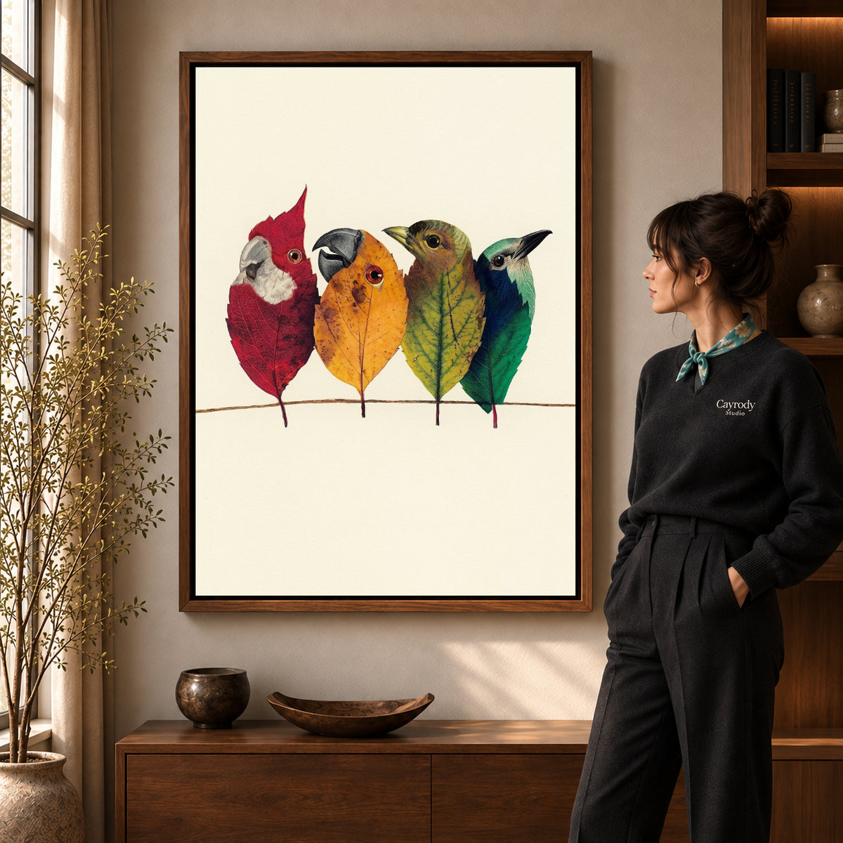 Autumn Leaf Birds artwork in a walnut frame beside a standing woman in a warm room.