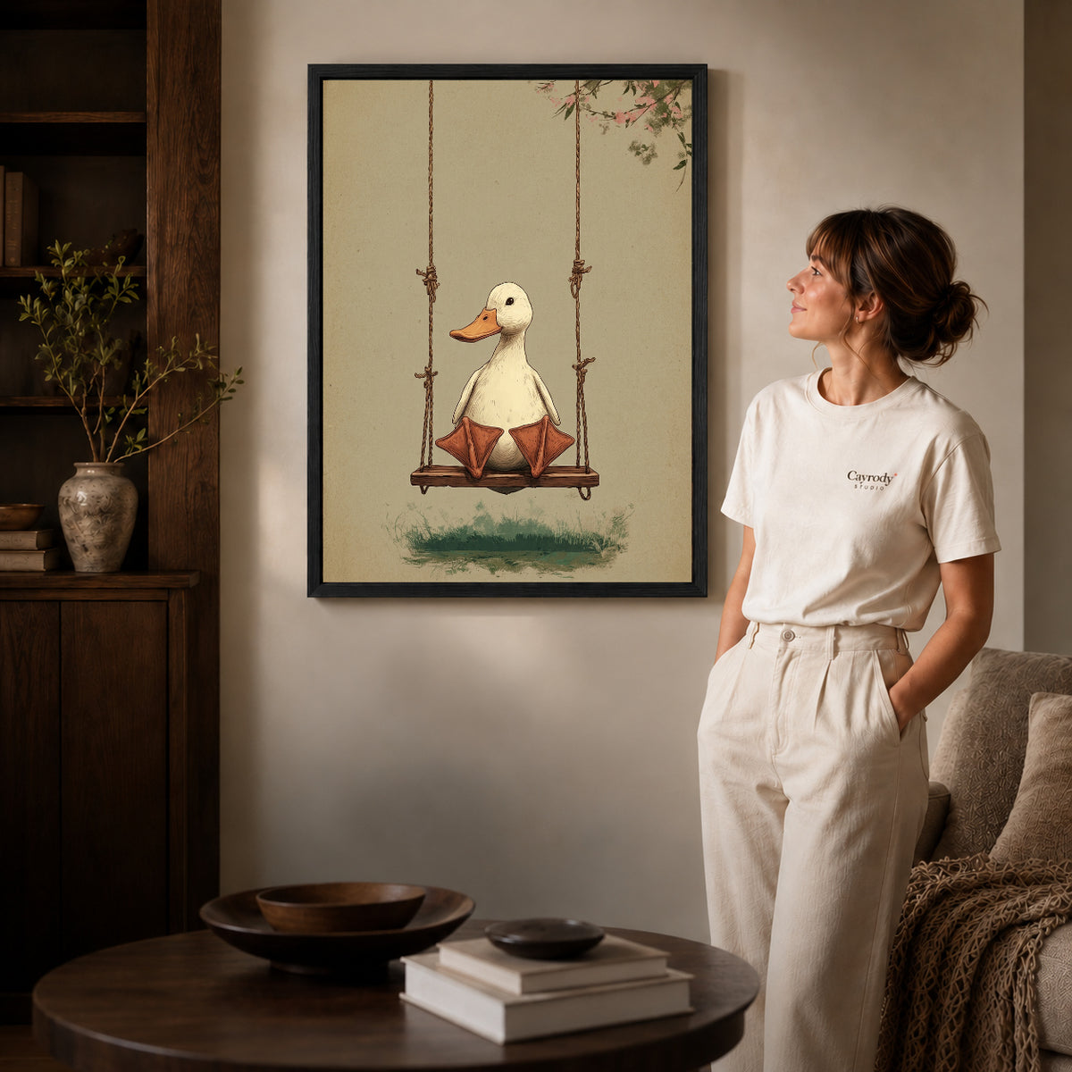Black framed swinging white duck artwork beside a woman in a warm neutral living room.