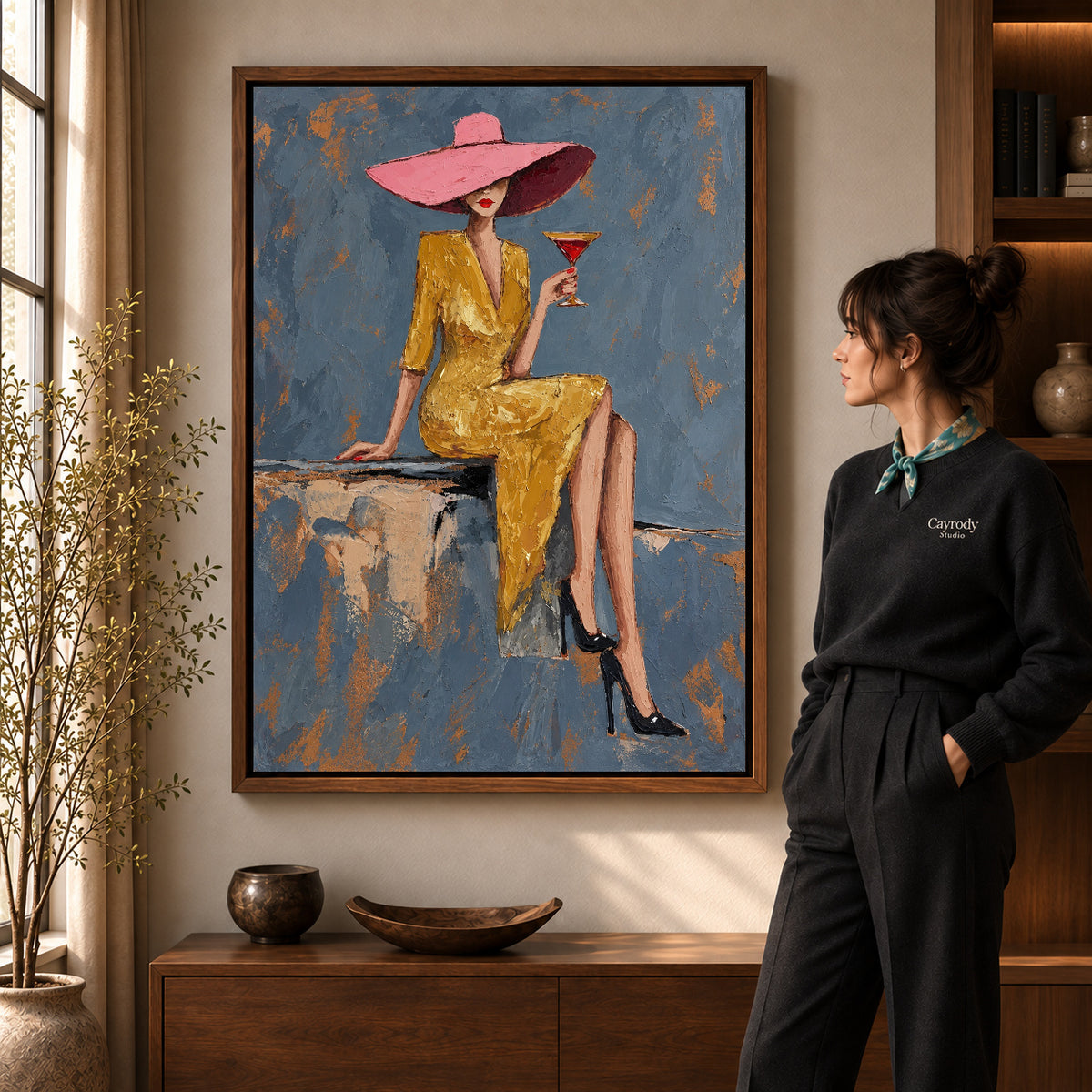 Pink Hat Elegance artwork in a walnut frame beside a standing woman in a warm room.