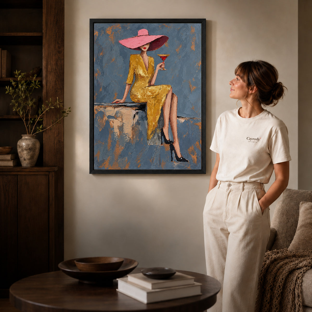 Black framed pink hat elegance artwork beside a woman in a warm neutral living room.