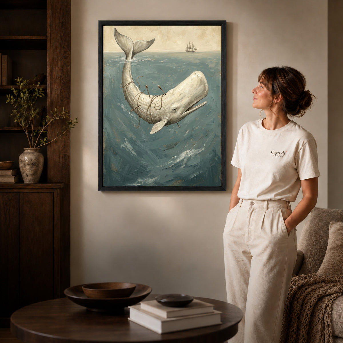 Black framed whale ocean voyage artwork beside a woman in a warm neutral living room.